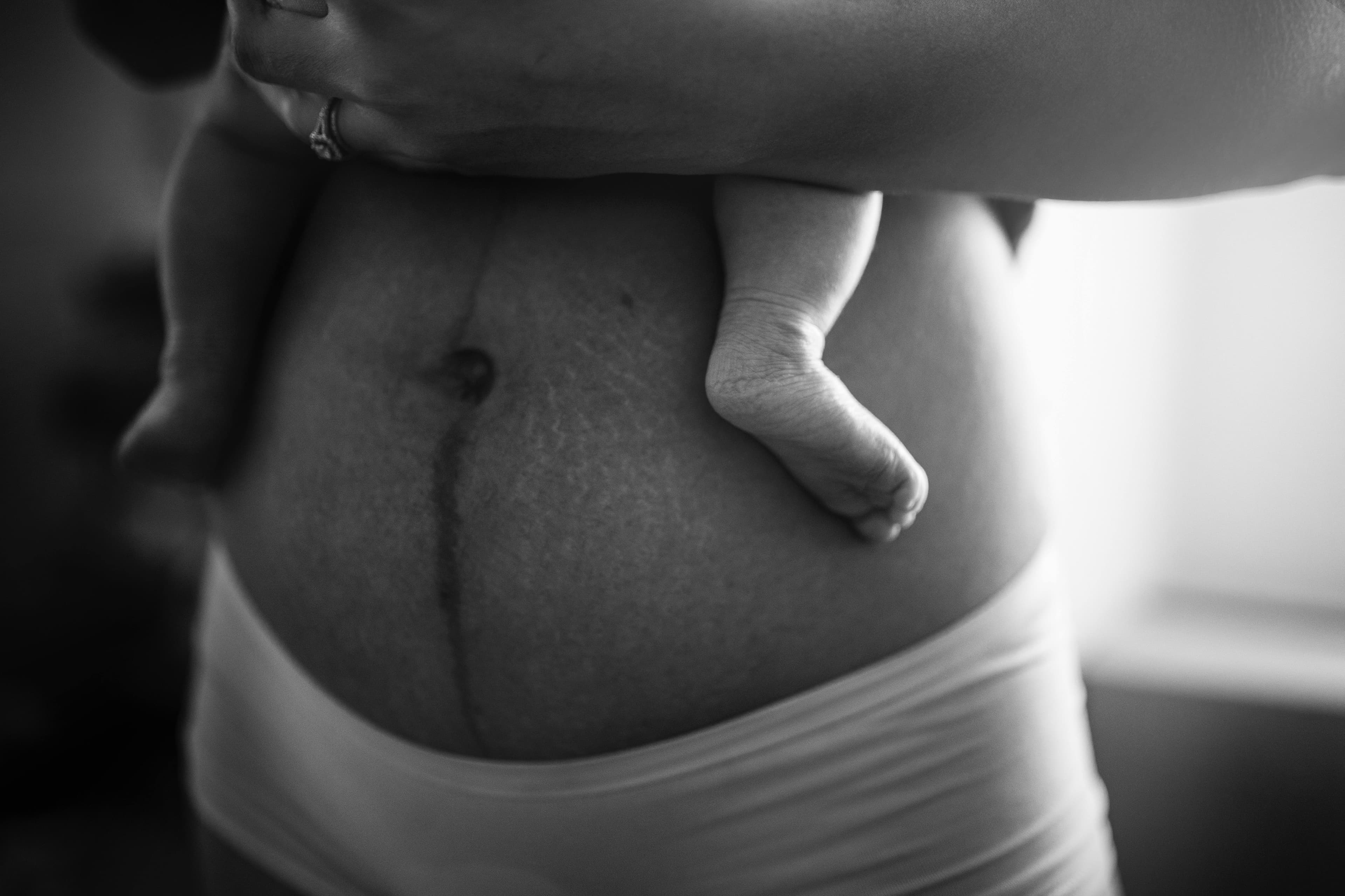 Postpartum belly with baby foot resting against it in black and white