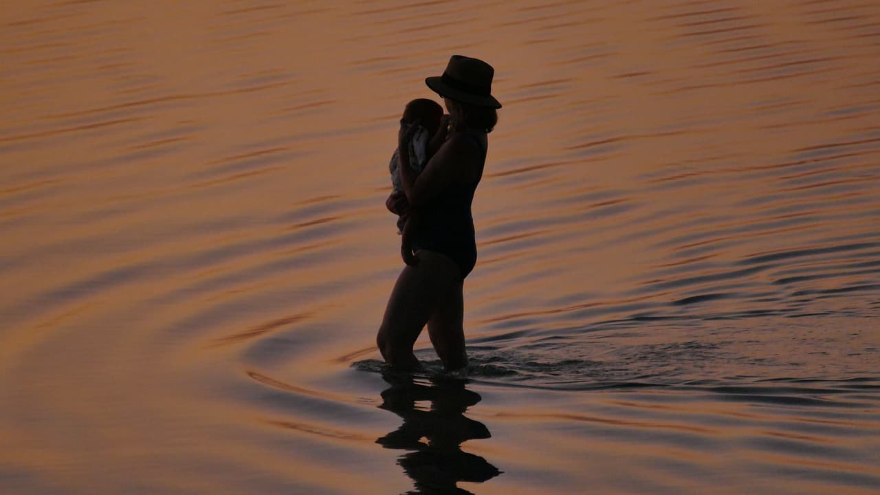 Mother silhouette holding baby in golden water at sunset